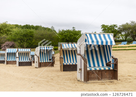 Row of vibrant striped beach chairs positioned on sandy ground surrounded by greenery creates a peaceful retreat for relaxation and leisure activities under cloudy skies 126726471