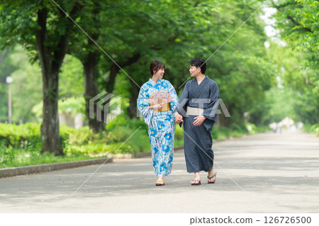 A couple in yukata walking along a tree-lined street 126726500