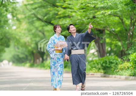 A couple in yukata walking along a tree-lined street 126726504