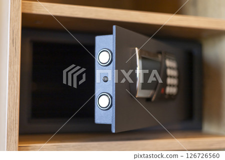 A secure safe with a digital keypad is partially open in a wooden cabinet. The safe has two circular buttons for operation and appears modern and functional 126726560