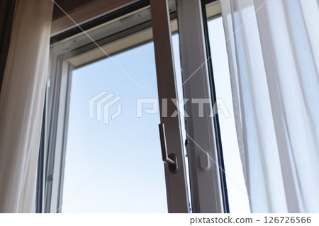 Soft sunlight filters into a room through an open window adorned with sheer curtains. The clear blue sky provides a bright, inviting atmosphere, suggesting a peaceful morning Soft sunlight filters into a room through an open window adorned with sheer curtains. The clear blue sky provides a bright, inviting atmosphere, suggesting a peaceful morning 126726566