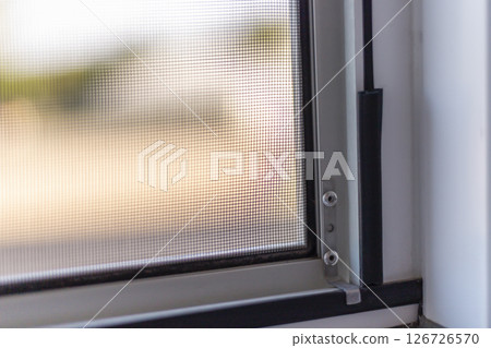 Sunlight streams through a fine mesh window screen, creating a warm and inviting indoor ambiance. The screen's details offer protection from flies while allowing light to filter in 126726570