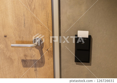 The entrance to a hotel room features a stylish door with a wooden panel and a sleek handle. A card key access device is mounted beside the door, ensuring secure entry for guests The entrance to a hotel room features a stylish door with a wooden panel and a sleek handle. A card key access device is mounted beside the door, ensuring secure entry for guests 126726631