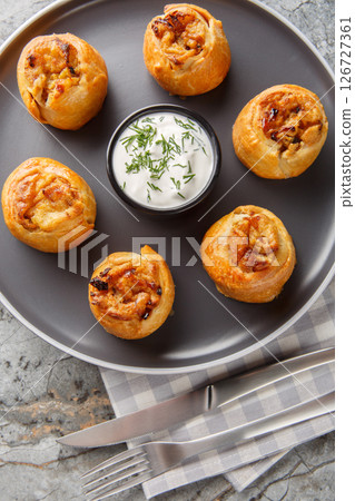 Ukrainian cuisine Knyshi pies with onion and potato filling served with sour cream close-up in a plate on the table. Vertical top view 126727361