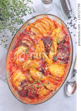 Gratin with sweet potato, parsnips, beet root and melted cheese, in glass dish, vertical top view 126727799