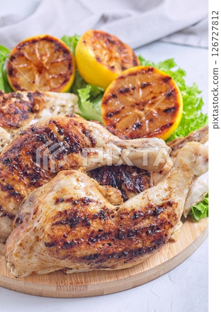 Grilled chicken legs and breast with lemon and lettuce on wooden board, vertical 126727812