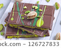 Dubai style milk chocolate bar with pistachio and kadaifi filing, lying on cutting board, horizontal 126727833