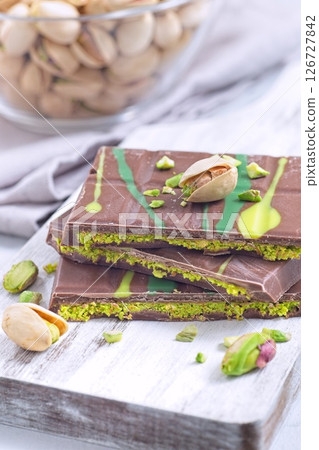 Dubai style milk chocolate bar with pistachio and kadaifi filing, lying on cutting board, vertical Dubai style milk chocolate bar with pistachio and kadaifi filing, lying on cutting board, vertical 126727842
