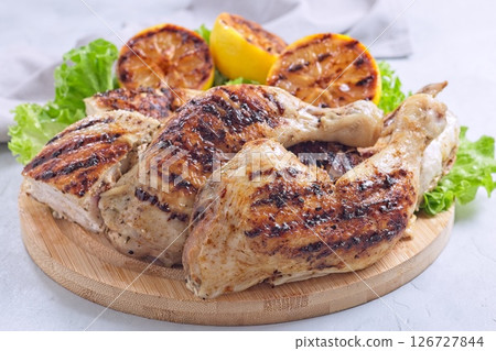 Grilled chicken legs and breast with lemon and lettuce on wooden board, horizontal 126727844