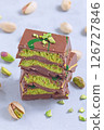 Stack of pistachio Dubai style chocolate bars with whole pistachios showing filling, vertical 126727846