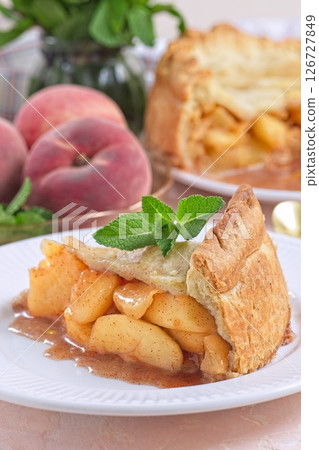 Delicious peach pie slice garnished with fresh mint, on white plate, vertical Delicious peach pie slice garnished with fresh mint, on white plate, vertical 126727849