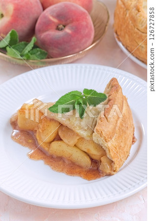 Old fashioned deep dish peach pie slice garnished with fresh mint, on white plate, vertical Old fashioned deep dish peach pie slice garnished with fresh mint, on white plate, vertical 126727858