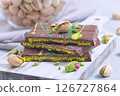 Delicious milk chocolate bar with pistachio and kadaifi filing, lying on cutting board, horizontal 126727864