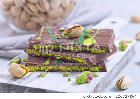 Delicious milk chocolate bar with pistachio and kadaifi filing, lying on cutting board, horizontal 126727864