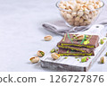 Milk chocolate bar with pistachio and kadaifi filing, lying on cutting board, horizontal copy space 126727876