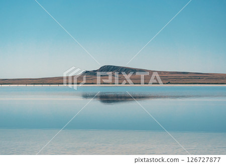 Baskunchak Lake salt flats reflect the vast blue sky and nearby hills in a serene landscape of natural beauty Baskunchak Lake salt flats reflect the vast blue sky and nearby hills in a serene landscape of natural beauty 126727877