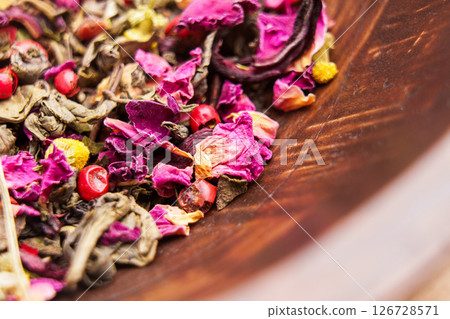 Herbal green tea with mixed ingredients hibiscus petals and chamomile flowers in a wooden bowl. Macro shot.  126728571