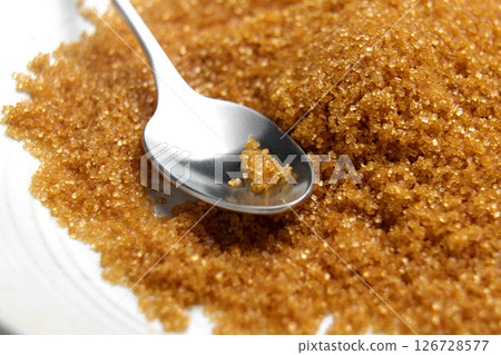 Organic brown cane sugar in a bowl with metal spoon. Scattered sweet ingredient. Macro shot.  126728577