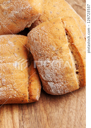 Fresh wheat bread buns with golden cracked crust on wooden table. Macro shot. Fresh wheat bread buns with golden cracked crust on wooden table. Macro shot. 126728587