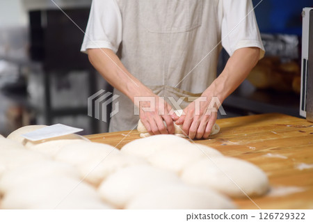 The bakery chef prepares the dough for baking bread. The baker kneads the dough and sets it to fit, baking eco-bread according to an old traditional recipe. Workflow in a local bakery 126729322
