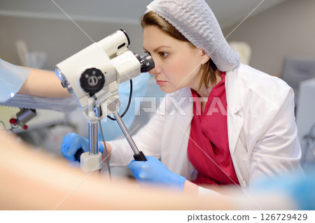 Gynecologist examines a patient using microscope in a gynecological chair. Doctor performs a colposcopy on a young girl in a modern medical office. Gynecologist examines a patient using microscope in a gynecological chair. Doctor performs a colposcopy on a young girl in a modern medical office. 126729429