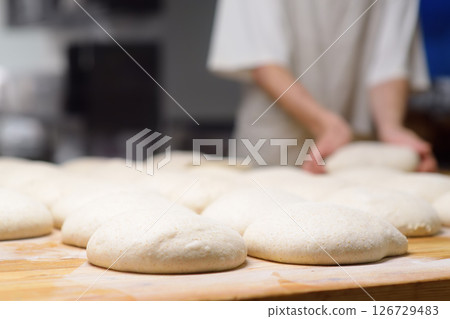 A batch of formed dough pieces on a table in the kitchen of a local bakery ready to bake. Olive ciabatta blanks laid out in a row in front of a large oven. Local bread production A batch of formed dough pieces on a table in the kitchen of a local bakery ready to bake. Olive ciabatta blanks laid out in a row in front of a large oven. Local bread production 126729483