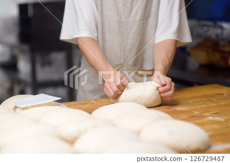 The bakery chef prepares the dough for baking bread. The baker kneads the dough and sets it to fit, baking eco-bread according to an old traditional recipe. Workflow in a local bakery The bakery chef prepares the dough for baking bread. The baker kneads the dough and sets it to fit, baking eco-bread according to an old traditional recipe. Workflow in a local bakery 126729487