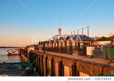 Scenic riverfront pier view at sunset, featuring boats and quaint cabins along the Volga River 126729914