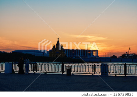 Sunset Silhouette: Two Women by Riverside, Cathedral, and Stadium 126729925
