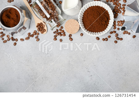 Coffee preparation scene featuring ground coffee, beans, milk, and tools arranged on a textured surface, creating an inviting atmosphere for enthusiasts 126731454