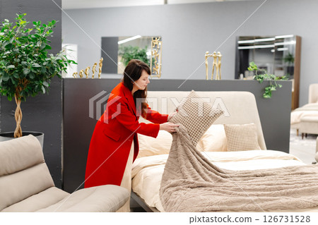 Interior designer arranging pillows on bed in furniture store 126731528