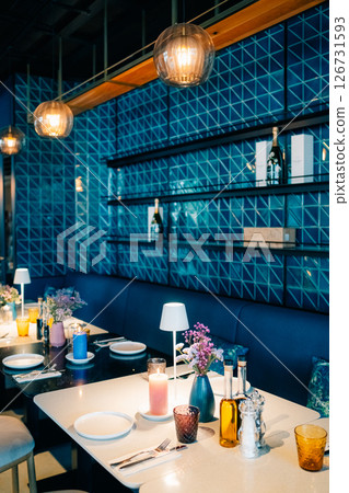 Elegant dining area with blue geometric decor and ambient lighting creating a cozy atmosphere in an upscale restaurant Elegant dining area with blue geometric decor and ambient lighting creating a cozy atmosphere in an upscale restaurant 126731593