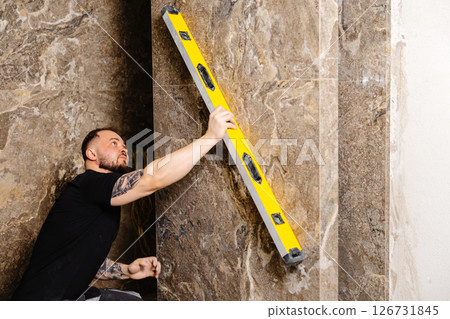 Construction worker using spirit level installing marble tile on wall 126731845