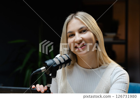 Smiling woman speaking into a microphone recording a podcast 126731980