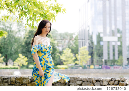 Young woman in summer dress is walking in green park and enjoying the sun. Playful and beautiful girl on warm sunny day. 126732040