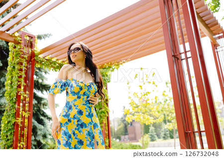 Beautiful young woman with long hair in trendy summer dress and sun glasses is walking in the park Beautiful young woman with long hair in trendy summer dress and sun glasses is walking in the park 126732048