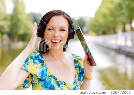 Attractive young woman with headphones listening to music via digital tablet a sunny day near lake Attractive young woman with headphones listening to music via digital tablet a sunny day near lake 126732062