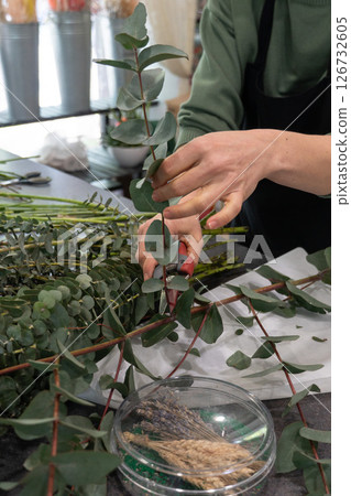 A florist trims eucalyptus branches at a workbench in a flower shop A florist trims eucalyptus branches at a workbench in a flower shop 126732605