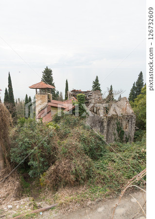A view of an abandoned building with a tower covered in ivy and a red-roofed house near the Black Sea in Gagra A view of an abandoned building with a tower covered in ivy and a red-roofed house near the Black Sea in Gagra 126732609