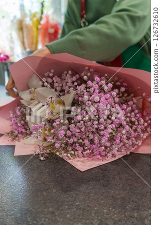 Close-up of a florist wrapping a bouquet of white orchids and pink baby's breath in pastel pink paper. Floral business 126732610