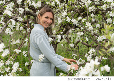 A woman in a light blue outfit stands among blooming apple trees. Mindfulness, connection with nature, mental well-being, and eco-lifestyle A woman in a light blue outfit stands among blooming apple trees. Mindfulness, connection with nature, mental well-being, and eco-lifestyle 126732615