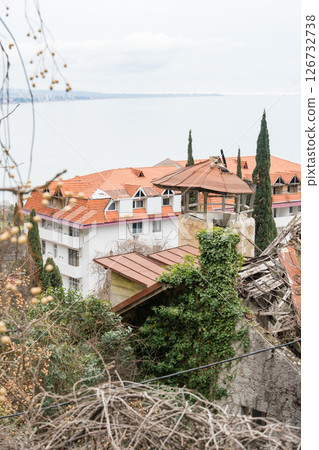 A view of an abandoned building with a tower covered in ivy and a red-roofed house near the Black Sea in Gagra A view of an abandoned building with a tower covered in ivy and a red-roofed house near the Black Sea in Gagra 126732738