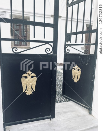 Black metal doors with a bird emblem - entrance to a church near the fortress in Santorini 126732816