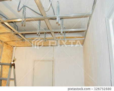 Installing ceiling metal frame with U-shaped brackets and mineral wool insulation for drywall - home renovation step Installing ceiling metal frame with U-shaped brackets and mineral wool insulation for drywall - home renovation step 126732880