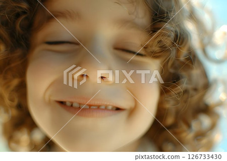 A young girl with curly hair is smiling with her eyes closed 126733430