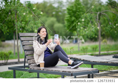 Woman making video call outdoors on lounge chair in park 126733931