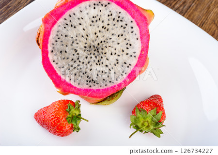 Close-up of half of pitahaya fruit on white plate with strawberries. Close-up of half of pitahaya fruit on white plate with strawberries. 126734227