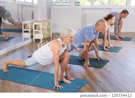 Mature female participant working out practice warrior pose, virabhadrasana with group Mature female participant working out practice warrior pose, virabhadrasana with group 126734412