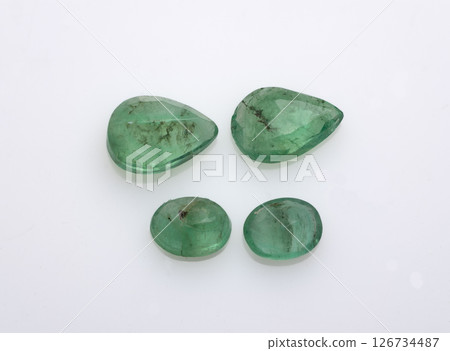 Collection of four natural, uncut emerald gemstones in varying sizes and pear-like shapes displayed against a clean white background, exhibiting varying degrees of inclusions and vibrant green hues 126734487