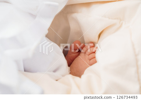 A close-up shot of a tiny baby's foot peeking out from under a soft, white blanket, evoking feelings of innocence, warmth, and new life 126734493